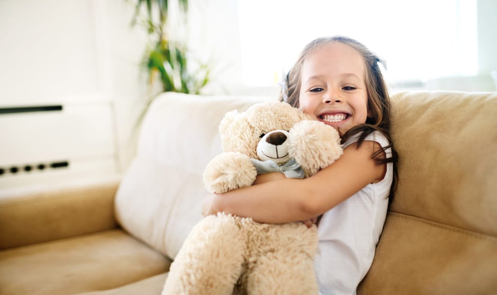 Eines lachendes Kindes, das mit einem Teddy kuschelt
